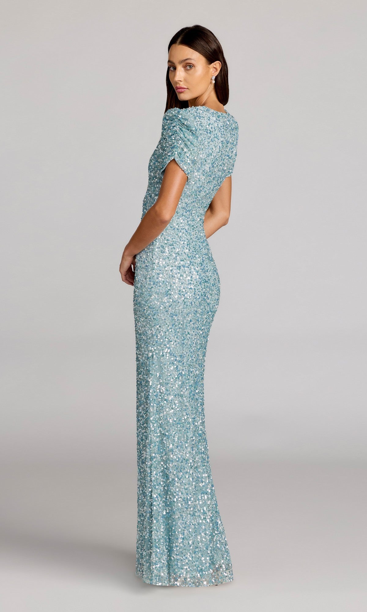 A woman faces sideways, wearing the Mac Duggal 24003 Short Sleeve Sequin Formal Dress in light blue, set against a neutral background.